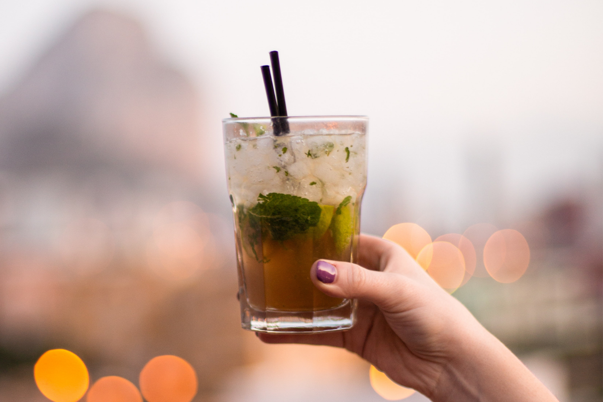 Mano che solleva un Mojito cocktail con due cannucce