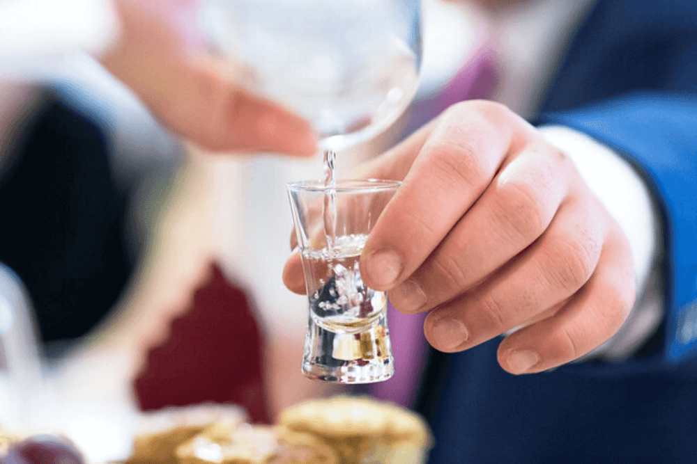 uomo mostra come si fa la vodka e come si serve nel bicchiere tradizionale